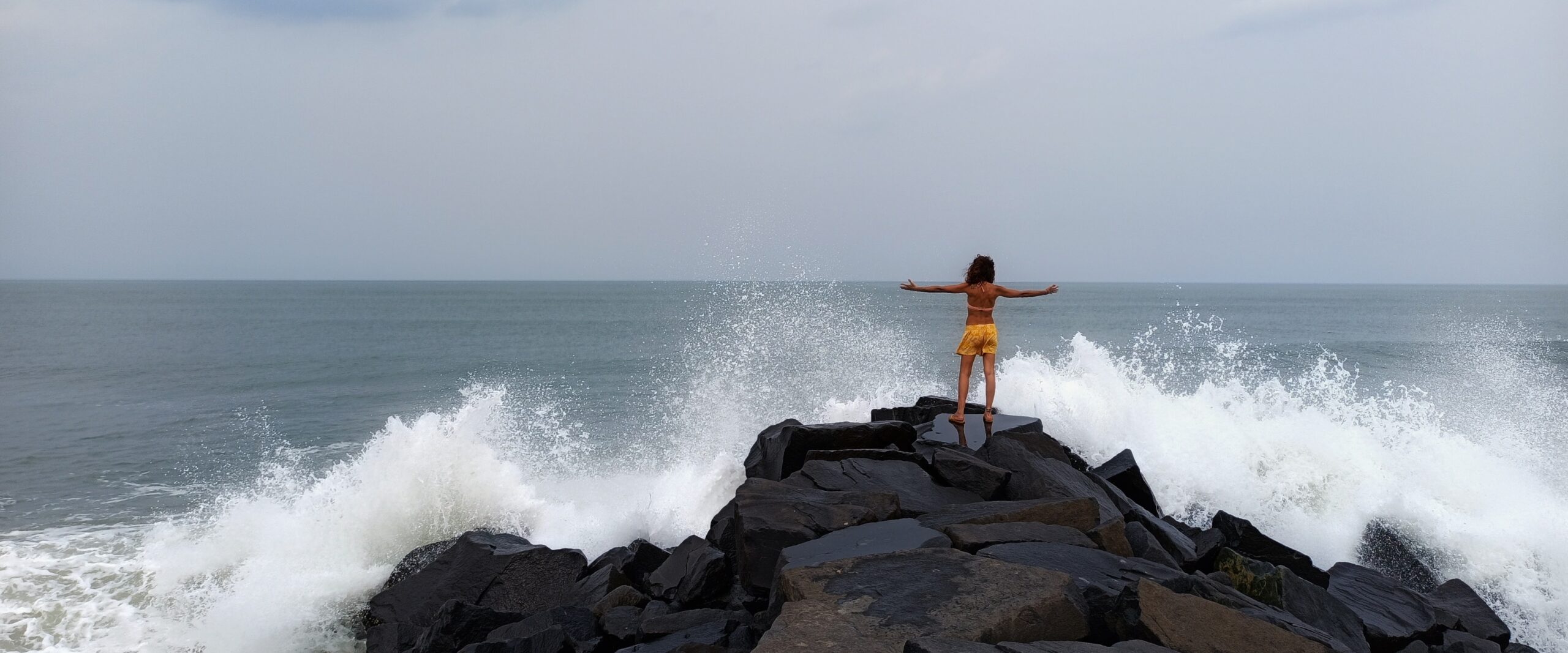 a woman standing on the ocean rocks welcoming the big waves